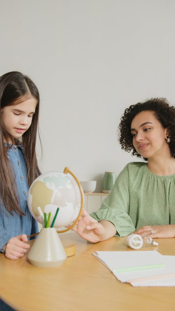 Young girl and woman exploring a globe together in an educational indoor setting.